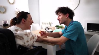 Genç erkek bakıcı, tekerlekli sandalyedeki engelli bir kadına glikoz izleme testi için yardım ediyor, şeker hastalığının tedavisi için empatik ve profesyonel bakım sağlıyor.