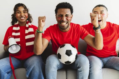Kırmızı tişörtlü ve yüz boyalı genç futbol fanatikleri evdeki kanepede çılgınca tezahürat yapıyor, eşarplar, megafon ve neşeli arkadaşlıkla büyük bir maçı kutluyorlar.