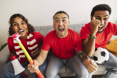 Kırmızı tişörtlü ve yüz boyalı farklı arkadaşlar heyecandan çığlık çığlığa bağırıyorlar, evlerinin rahatlığından birlikte futbol maçı izlerken birbirlerine bağlanıyorlar.