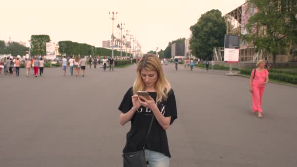 Rusland, Moskou - 23 juli 2016: De mooie blonde met iphones bladeren door foto's in het park Vdnkh — Stockvideo