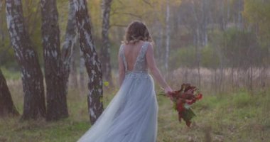 Gri gelinlik giymiş genç bir kadın düğününü kutluyor. Elinde çiçekler var ve şu an parkta..