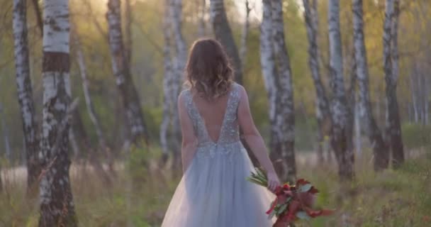 Een jonge vrouw gekleed in een grijze trouwjurk viert haar bruiloft. Ze heeft bloemen in haar hand en is in het park.. — Stockvideo