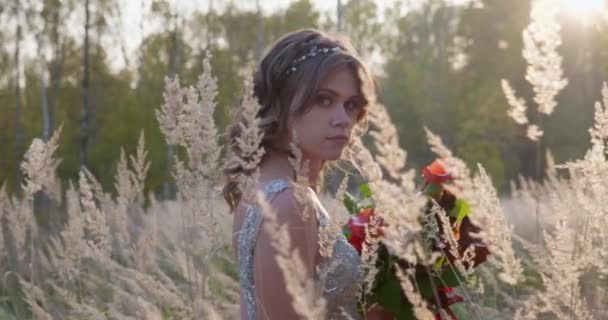 Молода жінка, одягнена у сіру весільну сукню. У неї в руці квіти і знаходиться в парку . — стокове відео