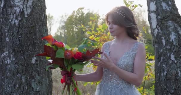Una joven vestida con un vestido de novia gris celebra su boda. Tiene flores en la mano y está en el parque.. — Vídeos de Stock