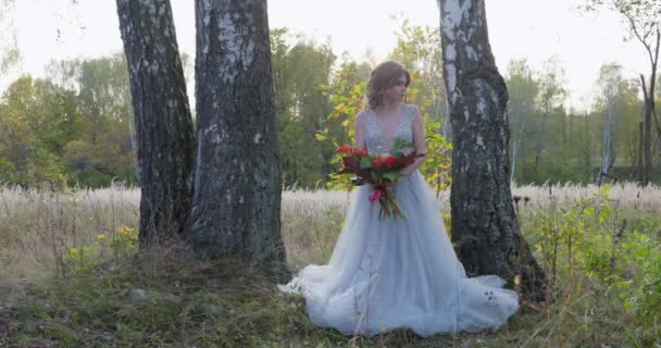 Μια νεαρή γυναίκα ντυμένη με γκρι νυφικό γιορτάζει το γάμο της. Έχει λουλούδια στο χέρι της και είναι στο πάρκο.. — Αρχείο Βίντεο