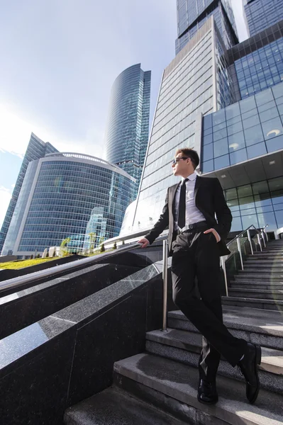 Empresário em pé nas escadas de um centro de negócios e olha para o lado . — Fotografia de Stock
