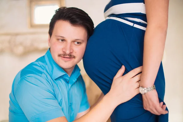Jovem pai ouvindo a barriga de uma esposa grávida — Fotografia de Stock