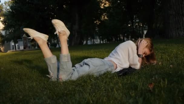 Modelo menina posando em jeans e blusa deitada no gramado . — Vídeo de Stock