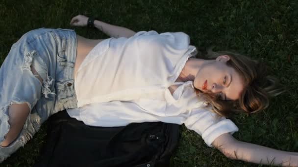 Modelo menina posando em jeans e blusa deitada no gramado . — Vídeo de Stock