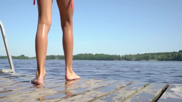 Girl in wetsuit jumping into the lake from wooden pier. Having fun on summer day. — Stock Video