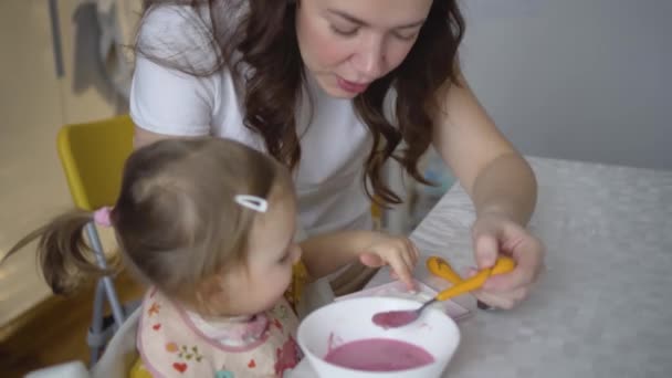 Niedliches Kind beim Essen. Das kleine Mädchen ernährt sich selbst gesund. Mutter füttert ihre kleine Tochter — Stockvideo