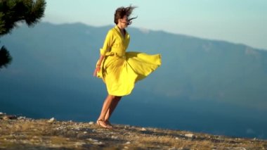 Sarı elbiseli güzel bir kadın dağın tepesinde atlıyor. Elbise ve saçlar rüzgarda savruluyor.