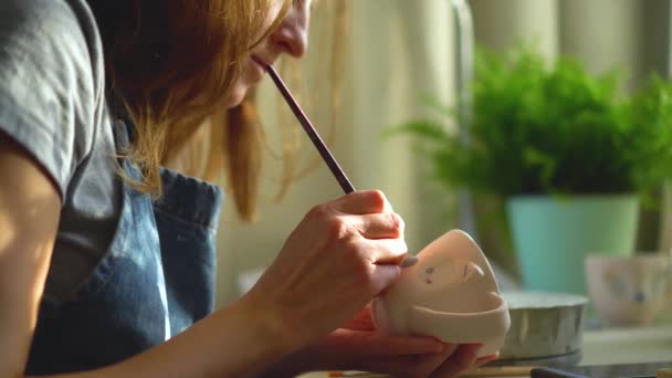 Vrouw die keramiek en aardewerk servies maakt in de werkplaats. jong meisje verft aardewerk met een borstel — Stockvideo