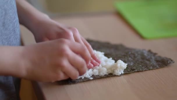 Kleiner Junge macht eine Maki-Rolle mit Algen, Lachs und japanischem Reis auf Sushi-Rollmatte. Junge bereiten traditionelle japanische Speisen zu. — Stockvideo