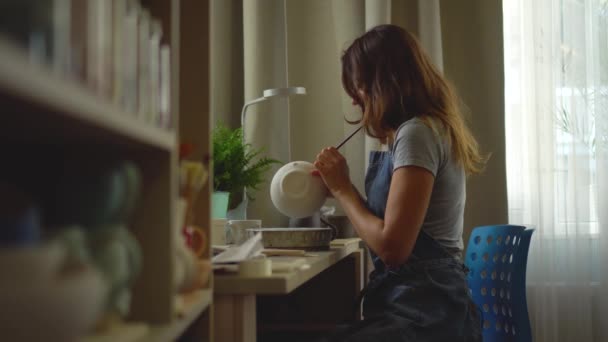 Vrouw die keramiek en aardewerk servies maakt in de werkplaats. jong meisje verft aardewerk met een borstel — Stockvideo