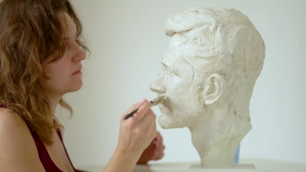 Beeldhouwer repareert gips sculptuur van mensenhoofd. Vrouw in de studio — Stockvideo