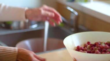 Bir kadın kevgirle böğürtlen yıkıyor. Beyaz ve kırmızı üzümlü. Görüntüyü kapat