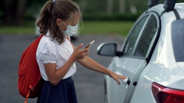 İlkokulda akıllı telefon kullanan sevimli öğrenciler. Güvenlik maskeli bir çocuk ve kız ellerinde aletlerle..