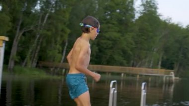 Tahta iskeleden göle atlayan dalgıç kıyafetli küçük çocuk. Yaz günü eğleniyorum..