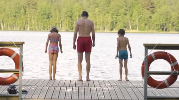 Lycklig familj har semester vid sjön. Far med dotter och son hoppar från piren tillsammans. — Stockvideo