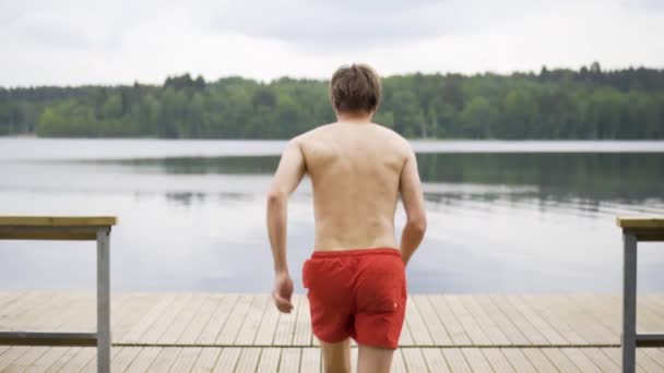 Junger Mann springt von Holzsteg in den See Spaß am Sommertag. — Stockvideo