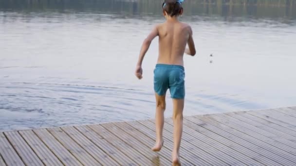 Kleiner Junge im Neoprenanzug springt von einem Holzsteg in den See. Spaß am Sommertag. — Stockvideo