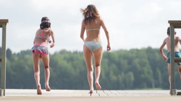 Šťastná rodina má dovolenou u jezera. Matka s dcerou a synem spolu vyskočí z mola. — Stock video