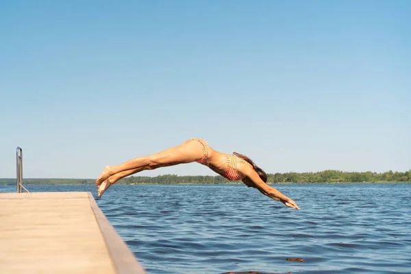 Женщина прыгает в озеро с деревянного пирса. Веселюсь в летний день. Молодая девушка ныряет в воду с причала. — стоковое фото