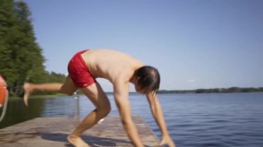 Ahşap iskeleden göle atlayan genç adam. Yaz günü eğleniyorum..