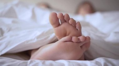 Yatakta beyaz çarşafların üzerinde bir çift ayak. Çocuk sabah yatağında yatar ve bacaklarını oynatır.