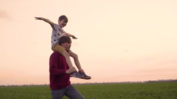 Barnet sitter på pappas axlar. Lycklig familj pappa med son spela tillsammans på fältet. Far och barn umgås i naturen — Stockvideo