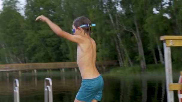 Kleiner Junge im Neoprenanzug springt von einem Holzsteg in den See. Spaß am Sommertag. — Stockvideo