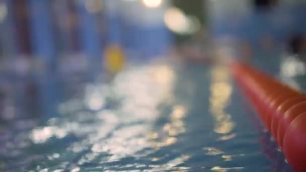 Wazig zicht op het sportzwembad. Focus op de voorgrond, op de rijstrookscheider. Een plan. Sprankelend water, bokeh — Stockvideo