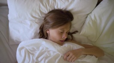 Uykulu kız, tatlı bir rüyadan sonra sabah erkenden uyanıp esniyor. Örtünün altındaki çocuk kameraya bakıyor.