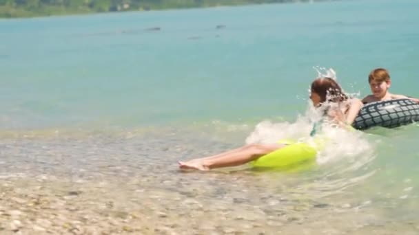 Niños felices nadando en agua azul en el mar. Vacaciones de verano. Chica y niño en anillos inflables paseo en ola de ruptura. Niños divirtiéndose en vacaciones — Vídeo de stock