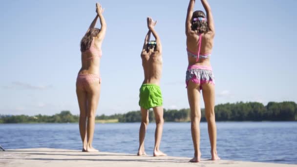 快乐的家庭在湖边度假。妈妈带着女儿和儿子一起从码头上跳了下来. — 图库视频影像