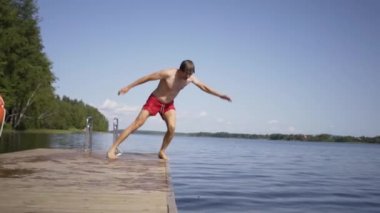 Ahşap iskeleden göle atlayan genç adam. Yaz günü eğleniyorum..