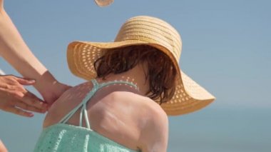 Anne, kızının omzuna güneş kremi sürüyor. Çocukların cildine güneş koruması.