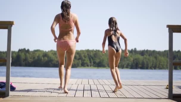 Glückliche Familien machen Urlaub am See. Mutter und Tochter springen gemeinsam vom Steg. Mädchen taucht vom Dock ins Wasser. Kinder haben Spaß — Stockvideo