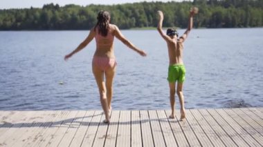 Mutlu ailenin gölde tatili var. Anne ve oğlu birlikte iskeleden atlıyorlar. Çocuk rıhtımdan suya dalıyor. Çocuklar eğleniyor.