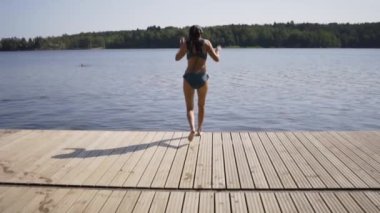 Ahşap iskeleden göle atlayan kadın. Yaz günü eğleniyorum. Rıhtımdan suya atlayan genç kız.