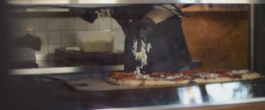 Şef pepperonili al taglio pizzasına parmesan peyniri sürüyor..