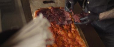 Şef geleneksel al taglio pizzasının üstüne pepperoni koyuyor. Yukarıdan aşağı, yavaş çekim..