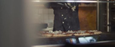 Şef pepperonili al taglio pizzasına parmesan peyniri sürüyor..