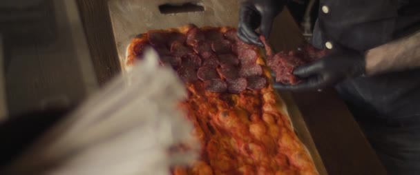 Chef plaçant pepperoni garniture sur une pizza traditionnelle al taglio. Plan du haut vers le bas, ralenti. — Video