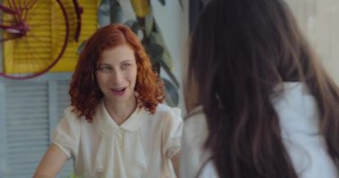 Renkli, modern bir kafede öğle yemeği molası verirken birbiriyle konuşan iki meslektaş. Yavaş çekim, orta çekim..