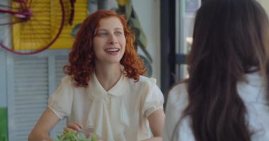 Renkli, modern bir kafede öğle yemeği molası verirken birbiriyle konuşan iki meslektaş. Yavaş çekim, orta çekim..