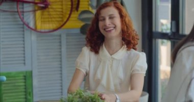 Renkli bir butik kafede kahve molasında gülen iki genç iş kadını. Yavaş çekim, orta çekim..