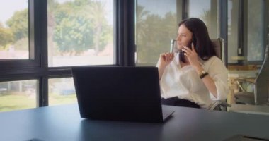 Ofiste çalışırken, beyaz bluzlu bir iş kadını telefonla konuşuyor. Ortalama çekim, yavaş çekim.