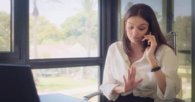 Ofiste çalışırken, beyaz bluzlu bir iş kadını telefonla konuşuyor. Ortalama çekim, yavaş çekim.